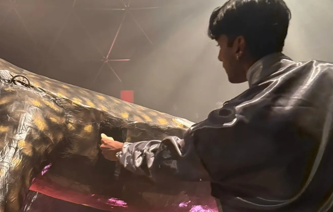 A man in a satin jacket posts a folded paper into an opening in the skink’s belly